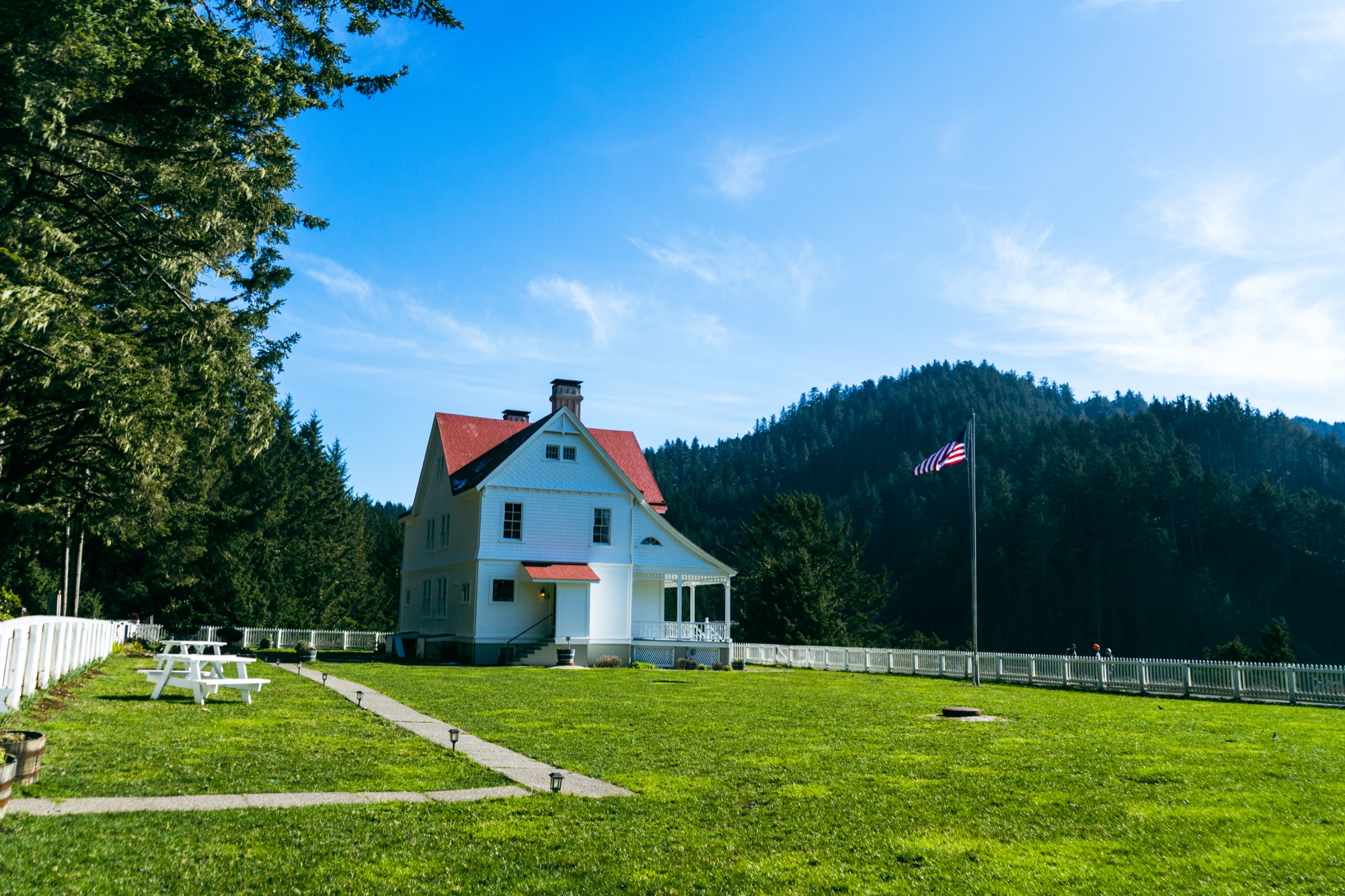 A white historic house on a broad lawn beneath forested hills.
