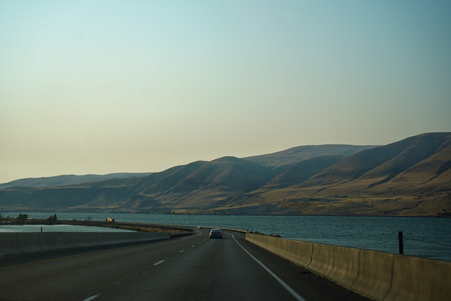 A highway curves beside a broad lake and rolling hills.